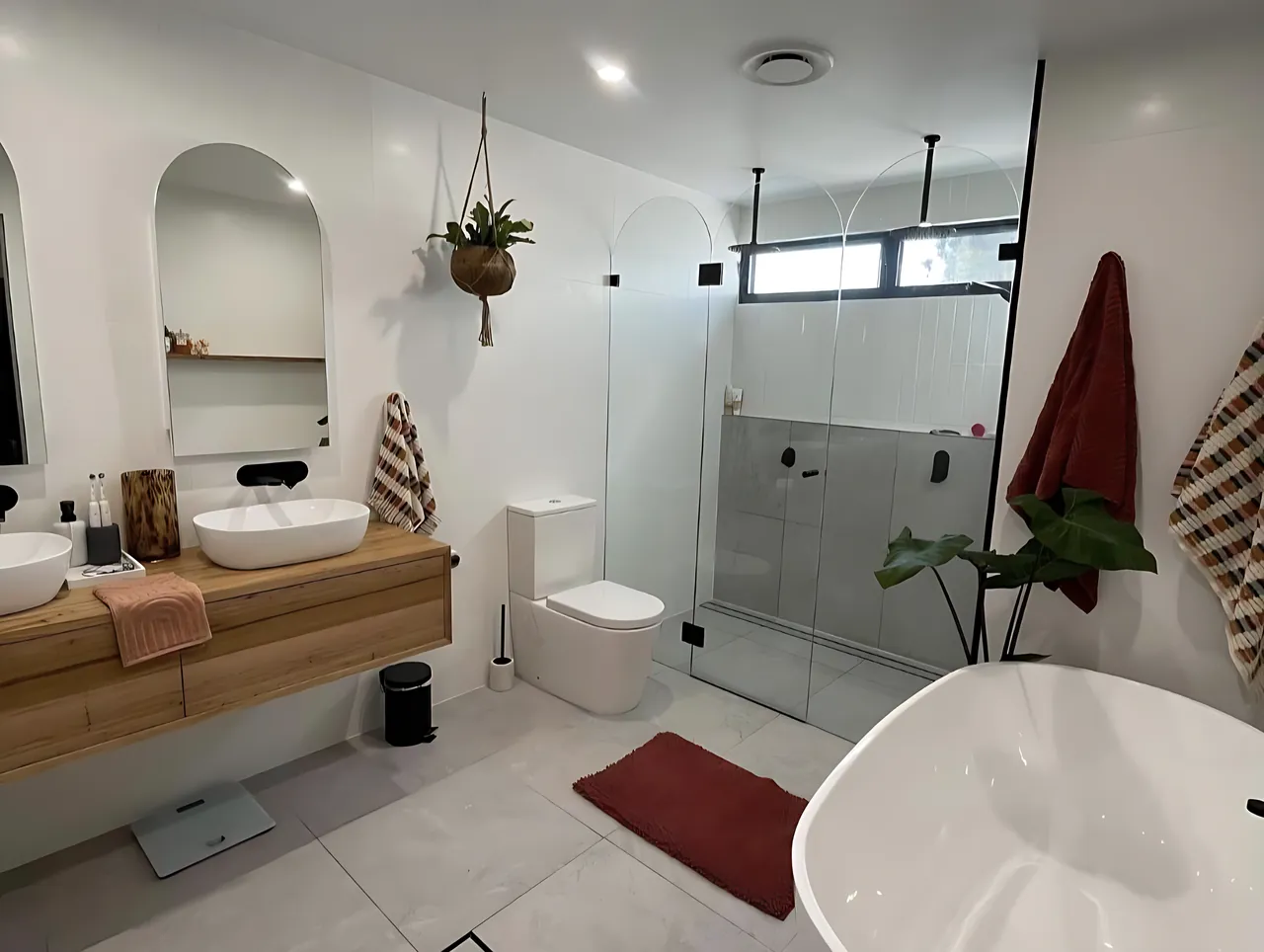 Bathroom renovation by Sunshower: timber floating vanity with twin basins, arched mirrors, a frameless arched shower screen and a freestanding bath