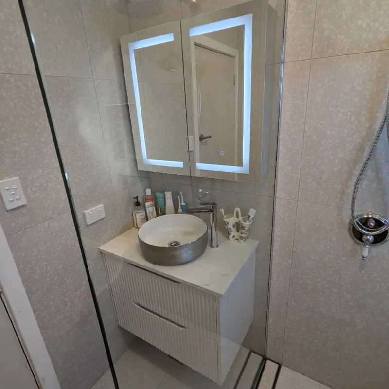 Wall-hung fluted vanity with a stone vessel basin under an LED shaving cabinet, against terrazzo-look tiles