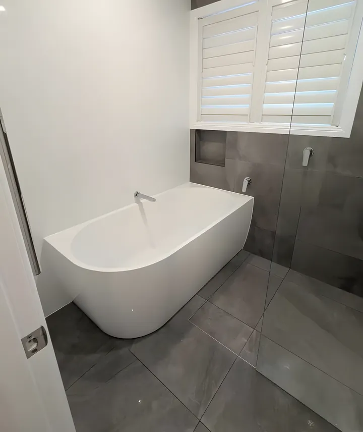 Charlestown bathroom: back-to-wall bath under the window beside a frameless shower, with large grey tiles on the floor and walls