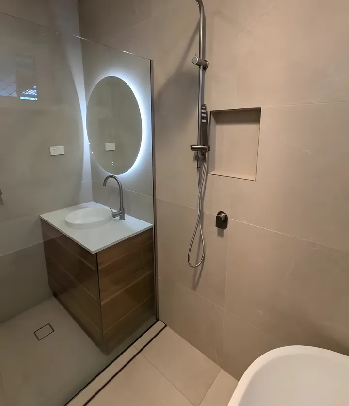 Garden Suburb bathroom: timber vanity under a backlit round mirror beside a frameless shower with a tiled niche