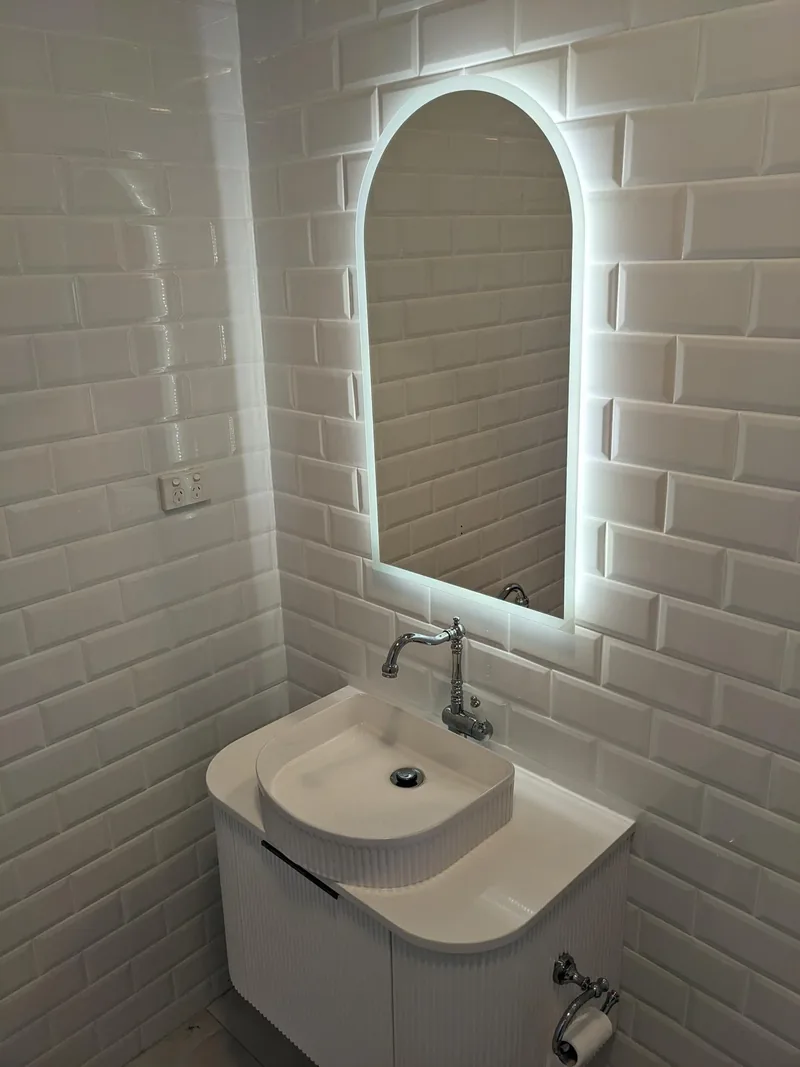 White bevelled subway tiles behind a curved vanity and arched backlit mirror