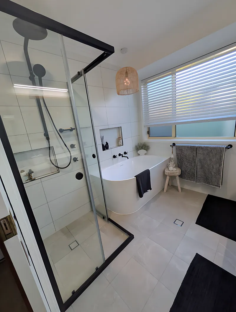 Bathroom renovation by Sunshower: black-framed shower with a tiled niche, a freestanding bath under the window and large-format floor tiles