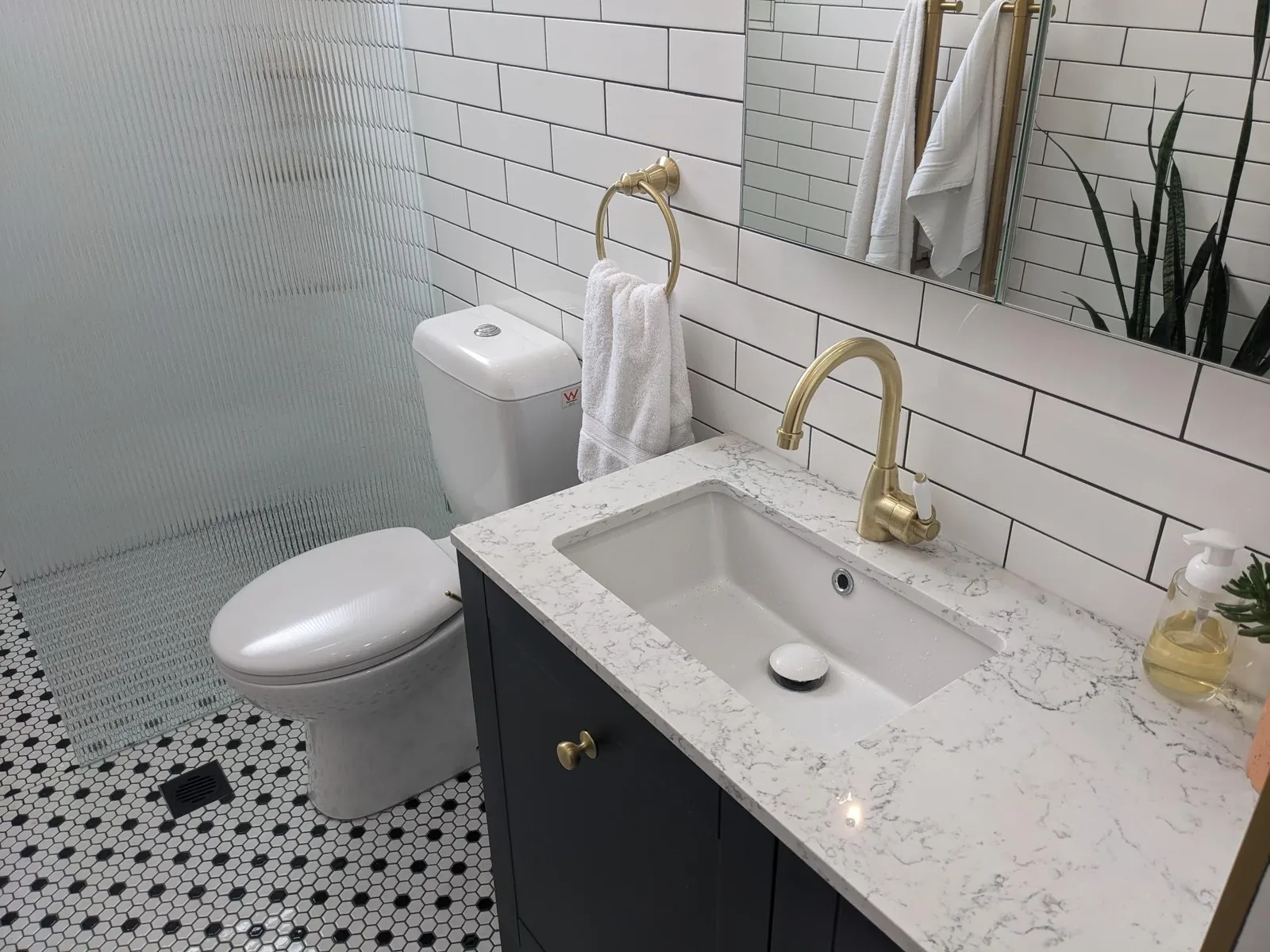 Hexagon mosaic floor and white subway tiles behind a navy vanity with brass tapware
