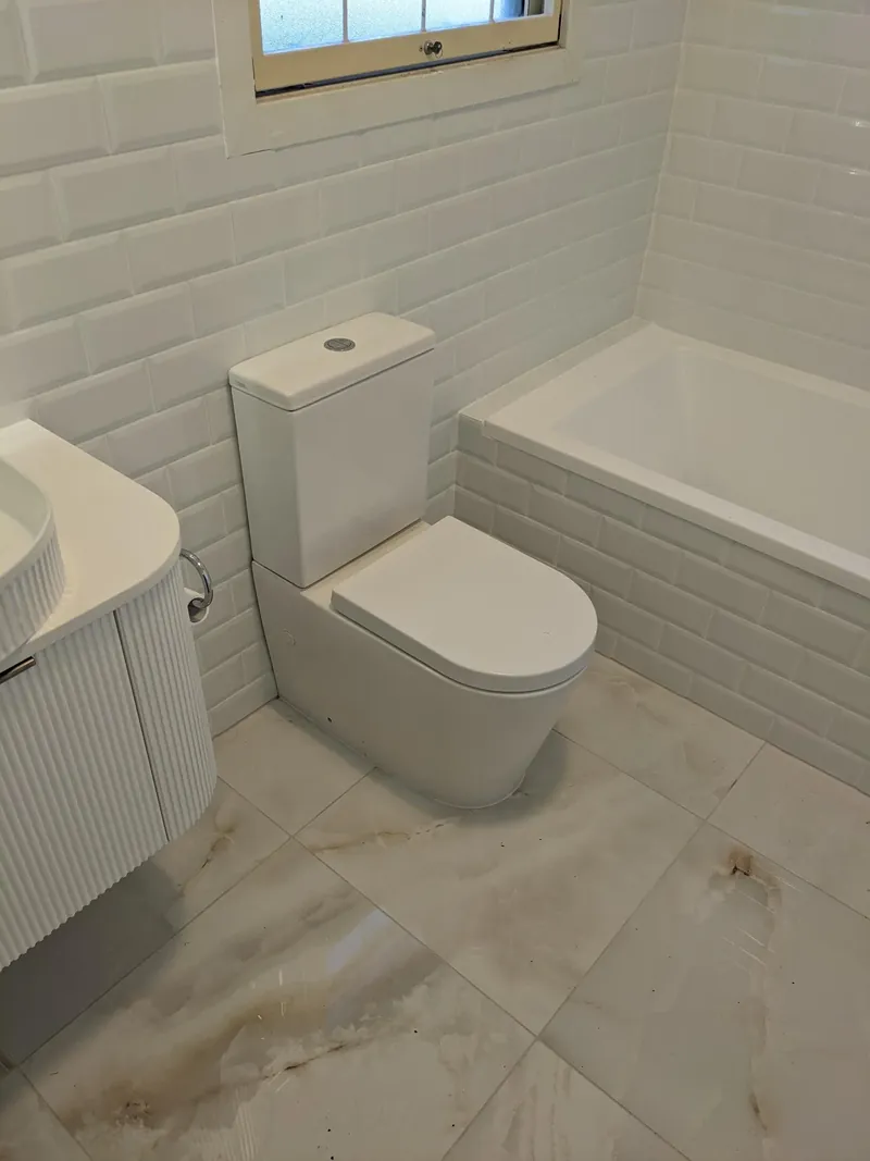Large marble-look floor tiles running under a wall-hung toilet and fluted vanity to a tiled bath hob