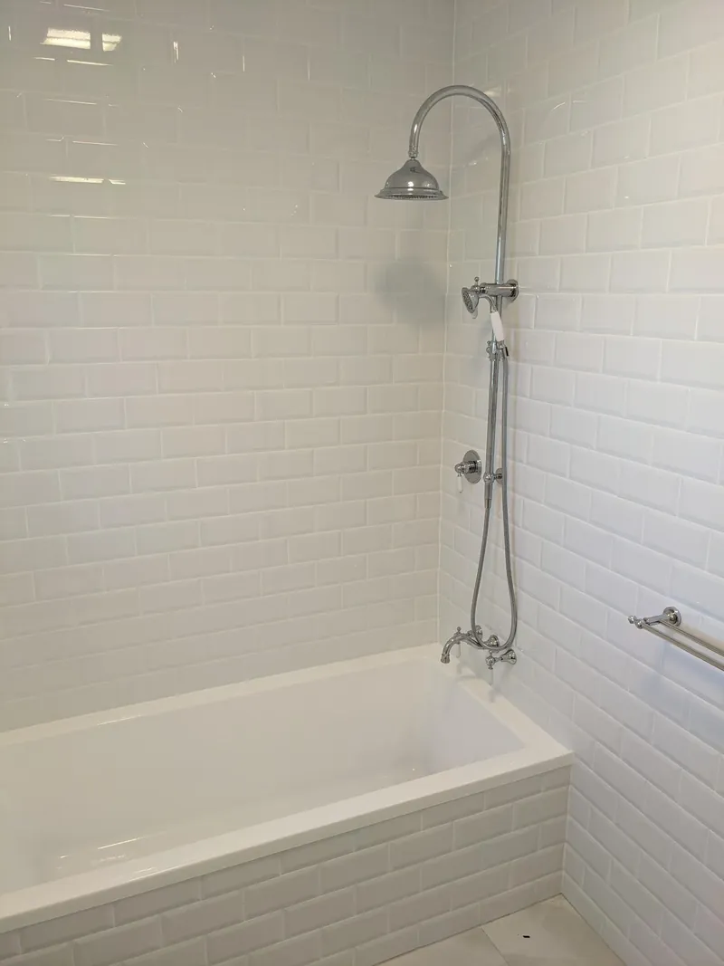 White bevelled subway tiles around a shower-over-bath with grey floor tiles