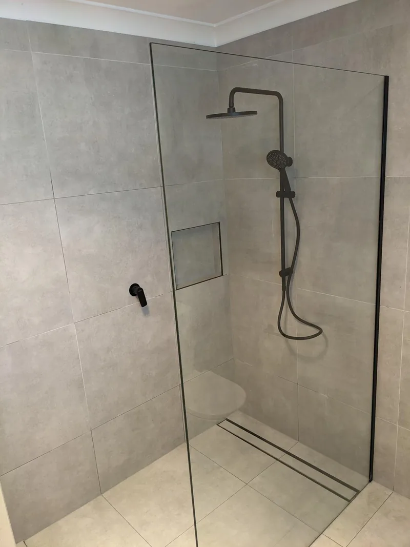 Walk-in shower with large grey wall and floor tiles, a tiled niche and a linear drain